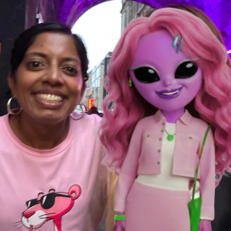 Sashi Perera smiling beside Pinkoma under a purple arch on an Edinburgh street